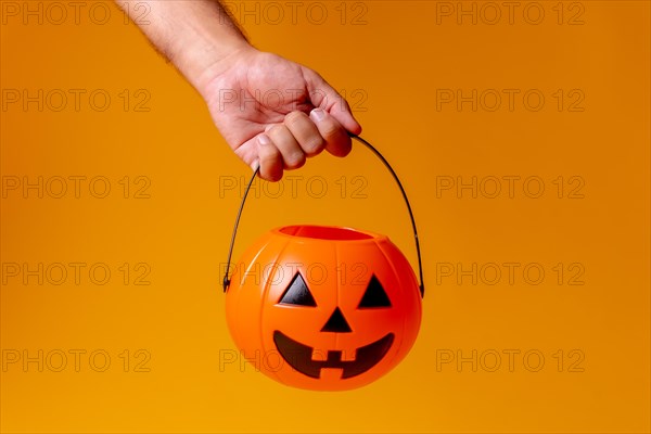 Hand holding an orange Halloween pumpkin on a background of yellow