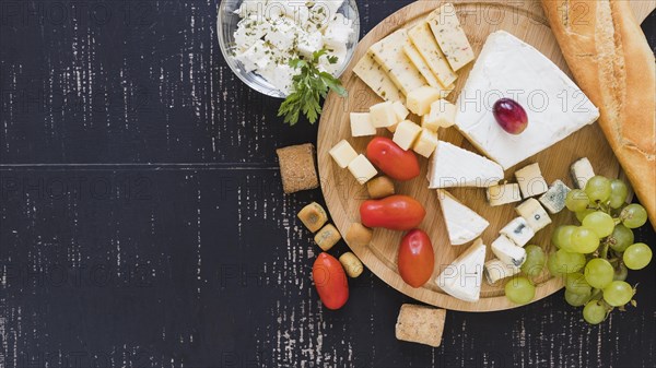 Cherry tomatoes grapes cheese blocks baguette round chopping board textured backdrop