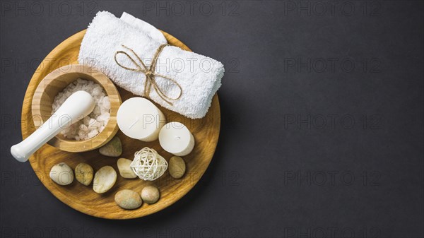 Elevated view salt towel candles spa stones wooden plate black backdrop