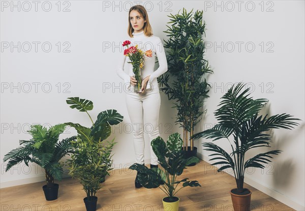 Thoughtful woman with flowers vase near green plant