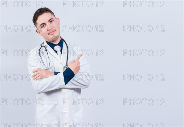 Smiling latin doctor pointing finger at a space isolated. Young doctor showing at a blank space. Doctor pointing at an isolated white space