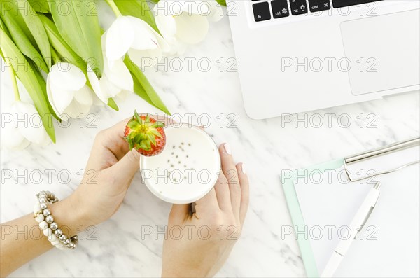 Woman holding yogurt drink near laptop