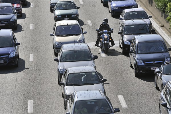 Motorcyclist riding between cars in traffic jam on motorway during the summer holidays