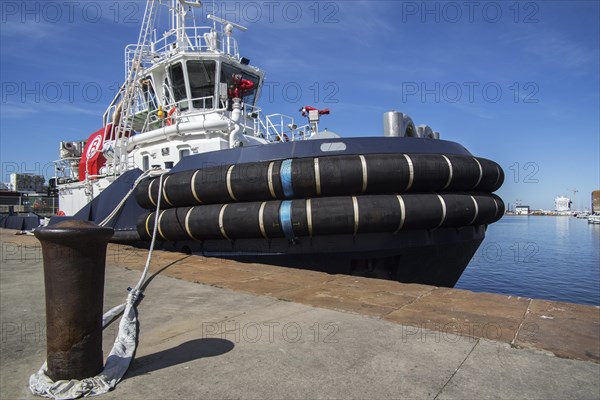 Mooring bollard and the French tug boat VB Mirage showing huge tugboat fenders docked in the seaport of Saint-Nazaire