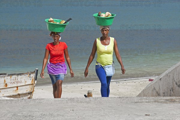 Two Creole women carrying plastic tubs with coconuts out of the harbour of Tarrafal on the island Santiago