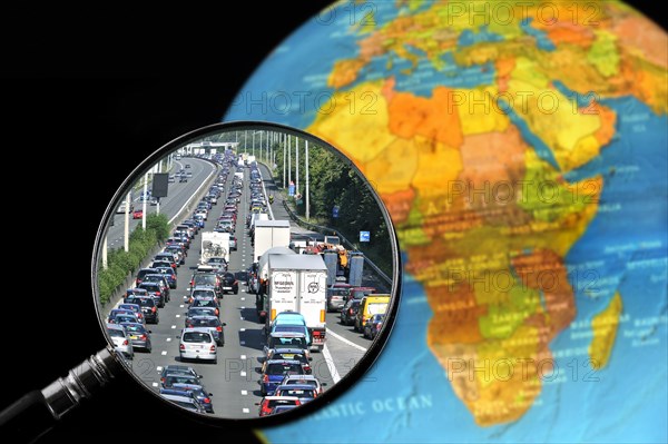 Cars in traffic jam on motorway during the summer holidays seen through magnifying glass held against illuminated terrestrial globe