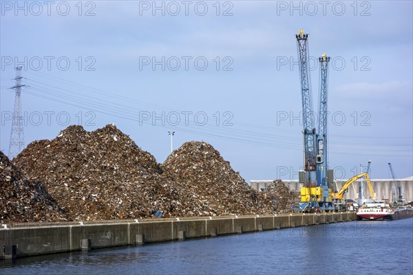 Dock cranes and heaps of recycled scrap metal at Van Heyghen Recycling export terminal in the port of Ghent