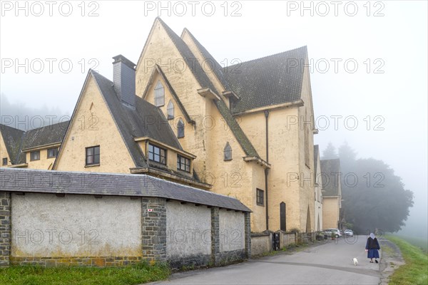 Cistercian nun walking her dog in front of the Abbaye Notre-Dame de Clairefontaine