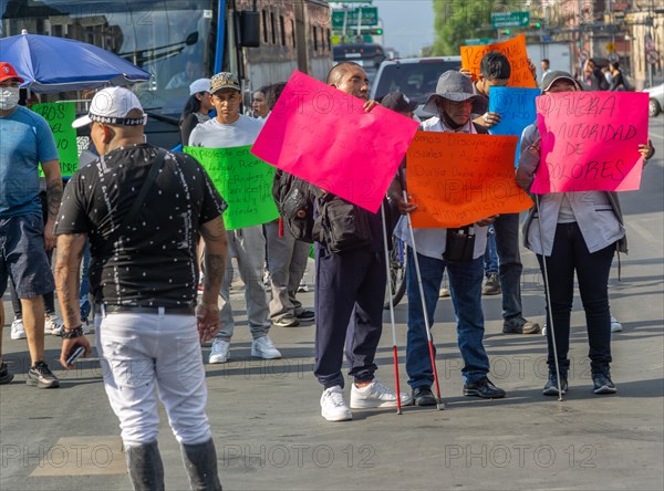 Blind visually impaired protestors holding placards block traffic on busy city centre road