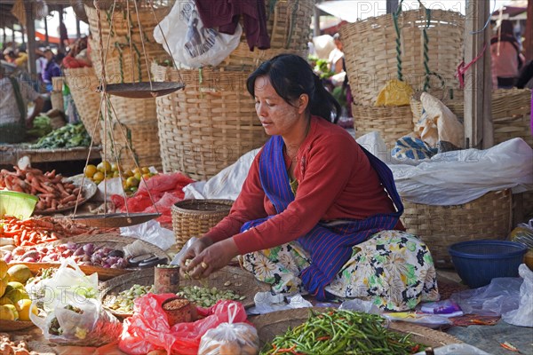 Female Intha vendor selling vegetables at weekly food market in lakeside village along Inle Lake