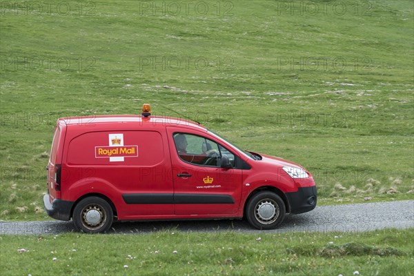 Postman driving red Peugeot Partner Royal Mail post van along desolate road in Shetland