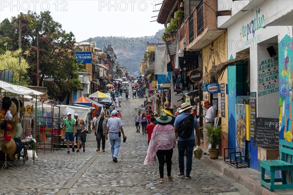 People walking along busy shopping street with mountain in distance