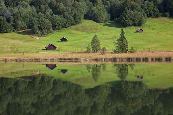 Wooden huts and reflection of pine forest in water along lake Gerold