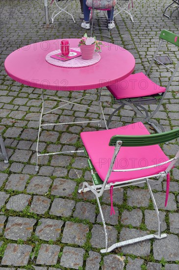 Pink table and folding chairs with pink cushions on cobblestone pavement