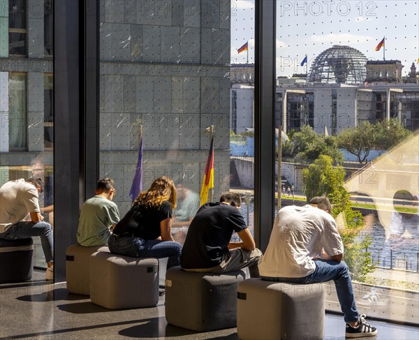 Museum visitors sitting at the window of the Futurium using their smartphones