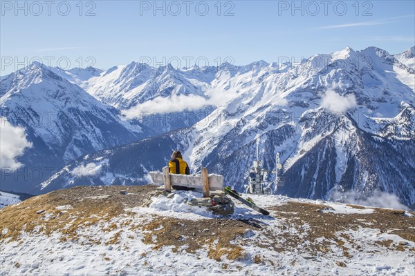 Skier sits on a bench and looks at the alpine chain