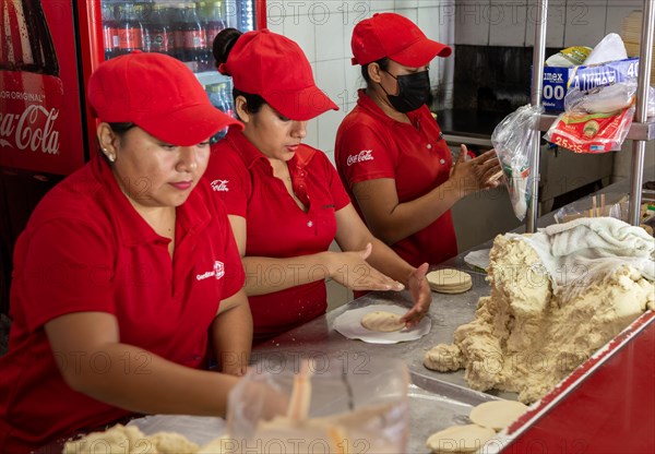 Woman rolling corn dough to make tortillas in gordita fast food cafe restaurant