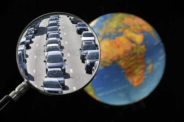 Cars in traffic jam on motorway during the summer holidays seen through magnifying glass held against illuminated terrestrial globe