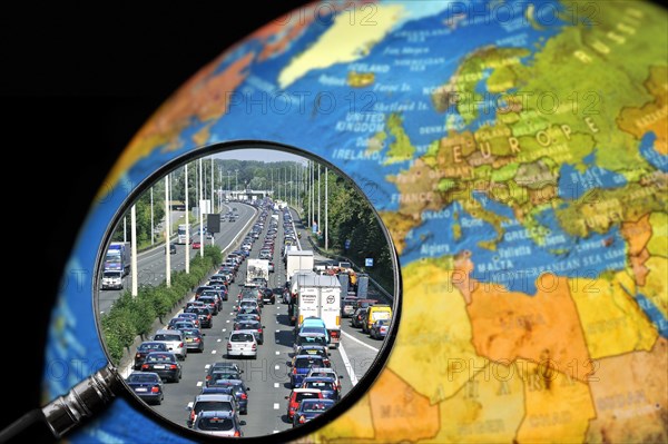 Cars in traffic jam on motorway during the summer holidays seen through magnifying glass held against illuminated terrestrial globe