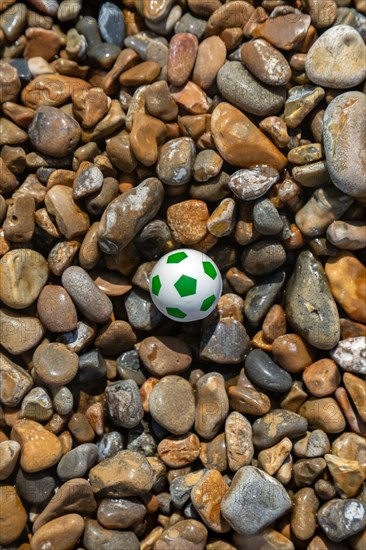 Miniature plastic football toy washed up on shingle beach