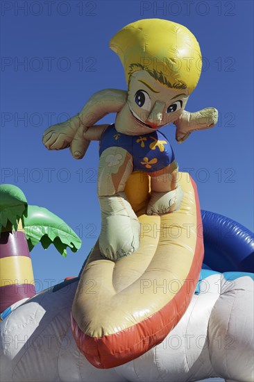 Inflatable bouncy castle with cartoon character Surfer on the beach