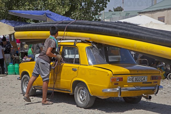 Uzbek boy fixing large pipes on top of old Trabant in Uzbekistan