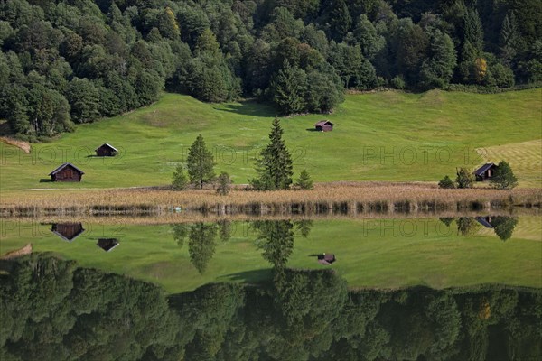 Wooden huts and reflection of pine forest in water along lake Gerold