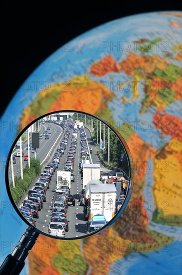 Cars in traffic jam on motorway during the summer holidays seen through magnifying glass held against illuminated terrestrial globe