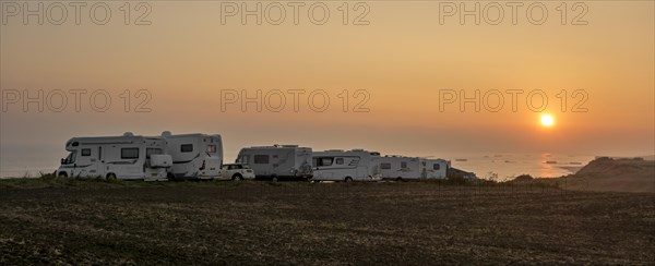 Motorhomes parked along the coast at sunset with view over the sea