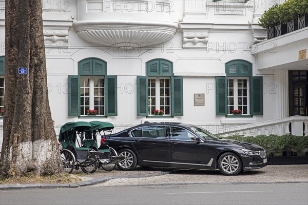 Rickshaws versus luxury car in front of colonial hotel in the capital city Hanoi