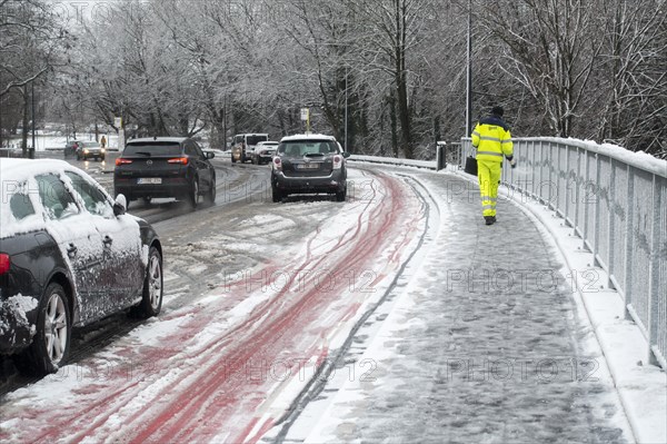 City worker spreading salt over slippery pavement on bridge covered in sleet during unexpected late snow shower in March 2023