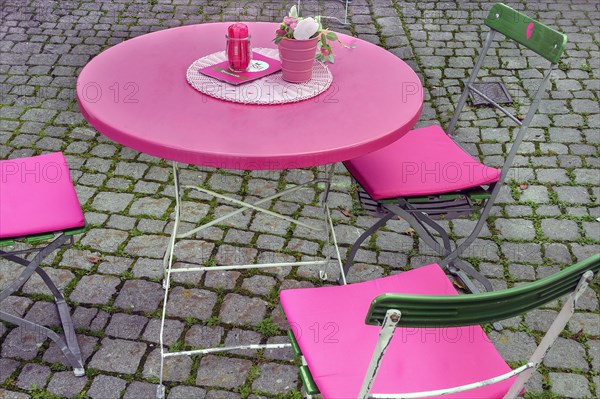 Pink table and folding chairs with pink cushions on cobblestone pavement