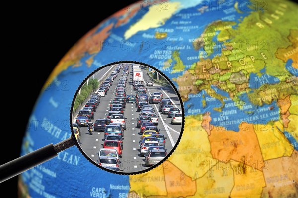 Cars in traffic jam on motorway during the summer holidays seen through magnifying glass held against illuminated terrestrial globe