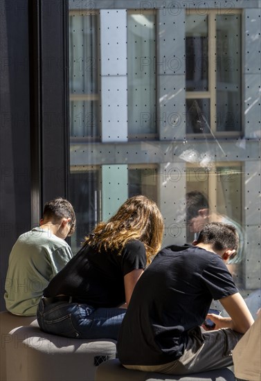 Museum visitors sitting at the window of the Futurium using their smartphones