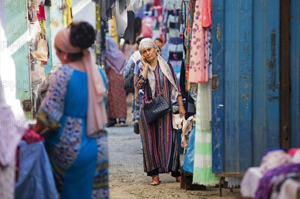 Kyrgyz woman with headscarf calling with smartphone at market in the city Osh