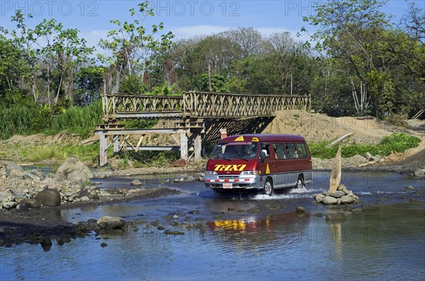 Taxi crossing river by driving through water next to unfinished bridge in Costa Rica