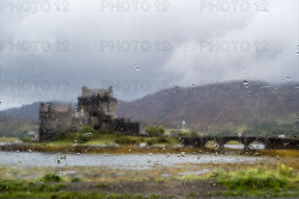 Eilean Donan Castle in Loch Duich seen through window with raindrops due to heavy rain