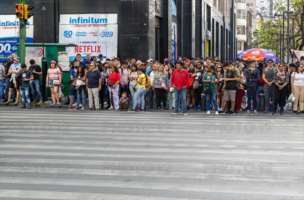 Large crowd of people waiting to cross busy road in city centre