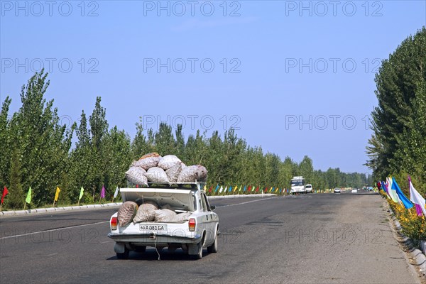 Car overloaded with large sacs stored on roof and in trunk driving along motorway in Uzbekistan