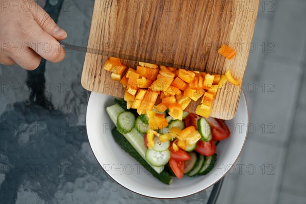 Top view of dropping chopped bell pepper from cutting board to a salad bowl