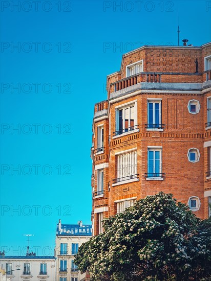 Beautiful orange brick building with a blooming tree at the bottom under a clear blue sky background in Asnieres-sur-seine a suburb of Paris