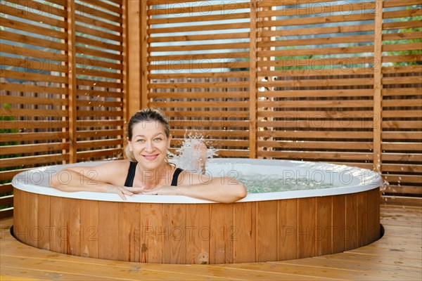 Happy woman relaxing in hot tub and dangles her feet in the water