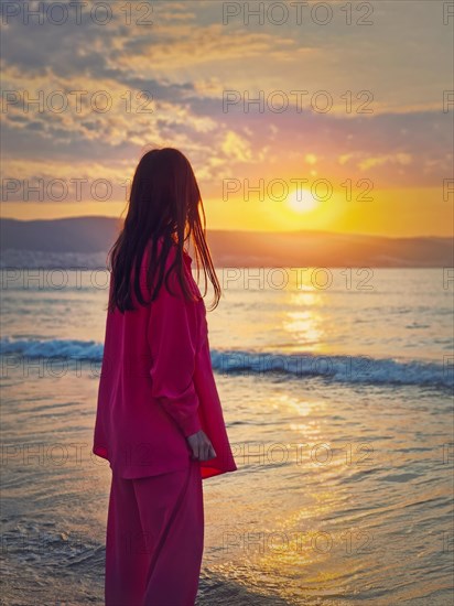 Aesthetic young woman rear view watching the sunrise above the hills at the sea. Beautiful dawn scene