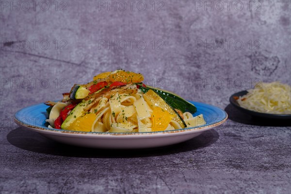 Tagliatelle pasta cooked with vegetables vegan recipe on a blue plate with grated cheese at the bottom