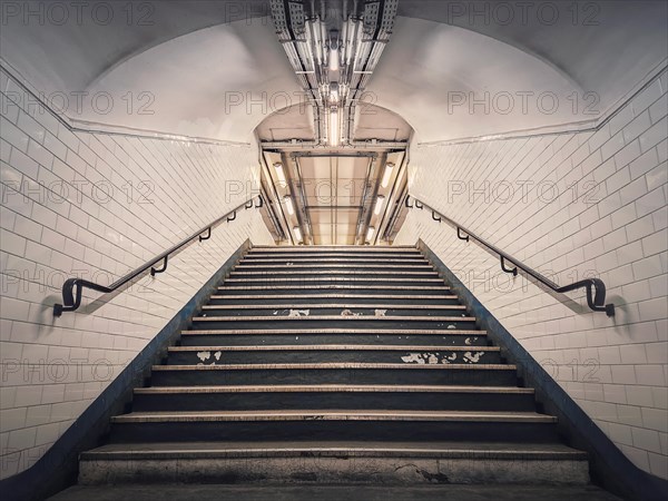 Subway corridor with white tile on walls and glowing lights above a the stairs passage. Symmetrical underground staircase