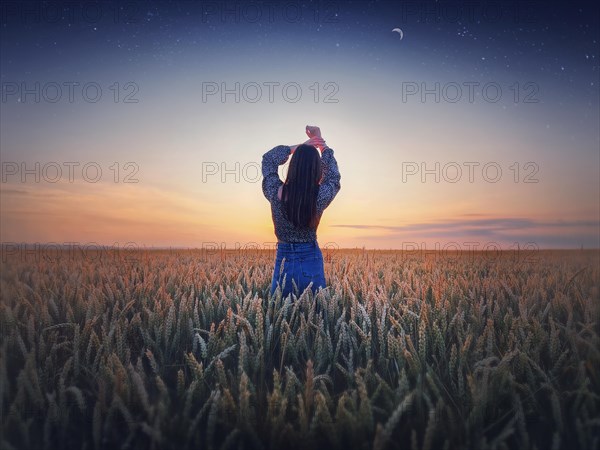 Girl in the golden wheat field at sunset. Beautiful twilight scenery under the summer starry sky with crescent moon. Magical natural scene