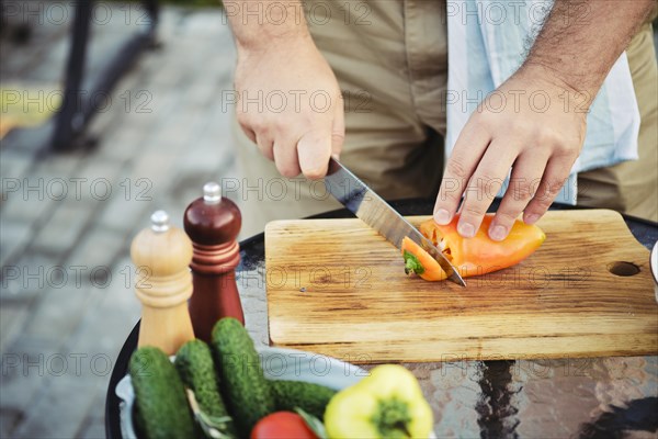 Unrecognizable man peeling sweet paprika with knife outdoors