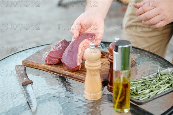 Unrecognizable man turning on other side raw beef strip steak to season it