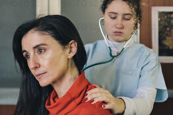 Young female physician performs a medical examination on a middle-aged patient. Lung auscultation for respiratory evaluation