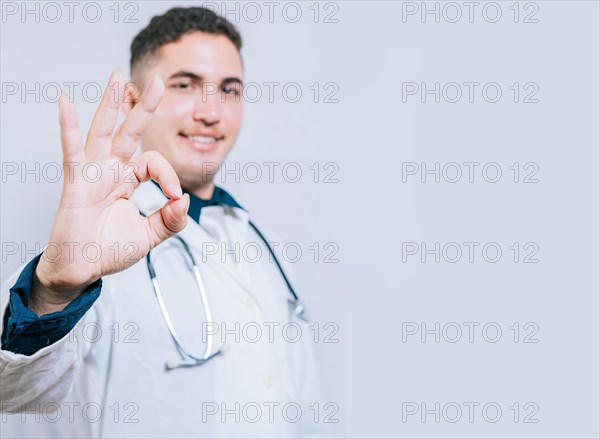 Handsome latin doctor approving and recommending isolated. Cheerful doctor gesturing approval isolated